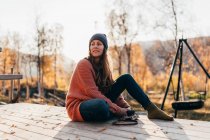 Брюнетка жінка, сидячи за допомогою камери на дерев'яну терасу в лісі і дивитися вбік — стокове фото