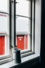 Белый керамический кувшин на белом подоконнике на фоне красного дома за окном . — стоковое фото