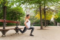 Вид сбоку атлетичной девушки растягивающей ноги на скамейке в парке — стоковое фото