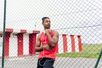 Retrato de atleta con auriculares sobre hombros apoyados en valla y mirando hacia otro lado - foto de stock