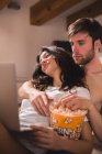 Homme avec popcorn embrassant femme naviguant ordinateur portable . — Photo de stock