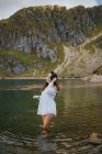 Усміхнена красива жінка стоїть в озері в схилі пагорбів і торкається волосся . — стокове фото