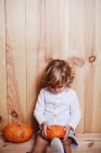 Petit enfant assis sur un fond en bois et regardant pensivement sur les citrouilles — Photo de stock