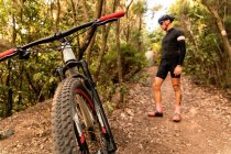 Человек в велосипедном шлеме позирует возле велосипеда в лесу — стоковое фото