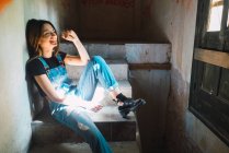 Смеющаяся девушка сидит и отдыхает на ступеньках заброшенного здания . — стоковое фото