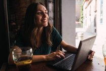 Portrait of cheerful woman sitting with laptop in cafe and looking aside — Stock Photo