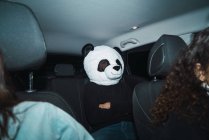 Hombre con máscara de cabeza panda sentado en el asiento trasero en el coche - foto de stock