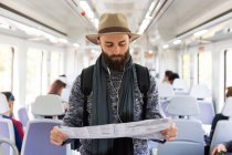 Turista barbuto con cuffie e mappa di lettura al treno pubblico . — Foto stock