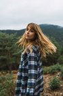Brunette girl in checkered shirt looking over shoulder at camera over forest on background — Stock Photo