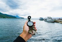Crop male hand holding compass over marine with moored boats — Stock Photo