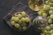 Непосредственный вид связки зеленого винограда в миске рядом с бокалом вина и бутылкой на столе — стоковое фото