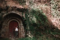Woman posing under door archway of medieval building with ivy covered wall — Stock Photo