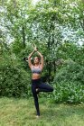 Jovencita en ropa deportiva de pie descalza sobre hierba verde en el parque realizando yoga asana y meditando . - foto de stock