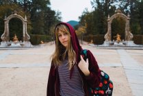 Brunette fille en sweat à capuche rouge marche avec sac à dos dans le parc — Photo de stock