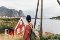 Вид сзади на женщину, наслаждающуюся видом на дом с травяной крышей над горным озером — стоковое фото