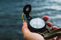 Crop male hand holding compass over sea waves — Stock Photo