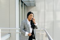 Lachende Geschäftsfrau in Jacke telefoniert auf Balkon eines Geschäftshauses — Stockfoto