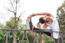 Athletic girl stretching leg on park fence — Stock Photo