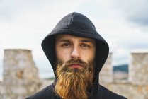 Portrait of young man with beard in black hood posing looking at camera. — Stock Photo