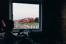 View of rural red cottages through window in dark room — Stock Photo