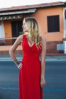 Retrato de mulher loira com penteado posando em vestido de noite vermelho na cena urbana e olhando para longe — Fotografia de Stock