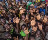 BENIN, ÁFRICA - AGOSTO 30, 2017: Baixo ângulo de sorrir crianças negras multidão gestos saudação com as mãos para cima e olhando para a câmera . — Fotografia de Stock