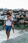 Portrait of man giving piggy back to girlfriend at seashore — Stock Photo