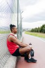 Vue latérale de l'athlète assis près de la clôture et se reposant après l'entraînement — Photo de stock