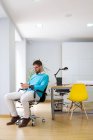 Ritratto di uomo d'affari seduto in sedia in ufficio moderno e smartphone di navigazione . — Foto stock