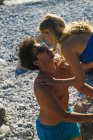 Woman bending to young man kissing him on rocky beach in sunlight. — Stock Photo