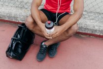 Crop sportsman sitting with bottle of water after workout — Stock Photo