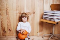 Little kid sitting on floor with pumpkinsand looking at camera — Stock Photo