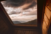 Драматический облачный пейзаж над горным ландшафтом через окно — стоковое фото