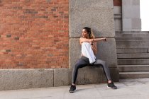 Sportliche Frau stützt sich auf die Schulter und wärmt sich auf der Straße auf — Stockfoto
