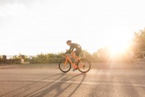 Vista lateral da bicicleta ciclista na estrada iluminada pelo sol no verão — Fotografia de Stock