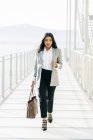 Vista frontale di donna elegante in giacca che trasporta borsetta e guardando la fotocamera sul passaggio balcone — Foto stock