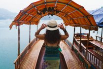 Rückansicht einer Frau, die ihren Hut auf einem Boot am See justiert — Stockfoto