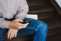 Crop man sitting on staircase and browsing smartphone — Stock Photo