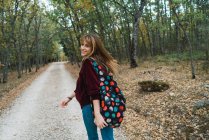 Brunette fille en sweat à capuche rouge marchant sur le chemin de la forêt et regardant par-dessus l'épaule à la caméra — Photo de stock