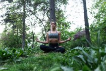 Низкий угол зрения спортивной женщины, сидящей на земле и медитирующей в парке — стоковое фото