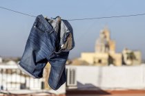 Blue jeans short hanging on clothesline over blurred cityscape — Stock Photo