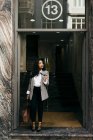 Stilvolle Frau verlässt Gebäude mit Sonnenbrille in der Hand und schaut zur Seite — Stockfoto