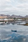 Маленькая лодка на озере над прибрежной деревней на заднем плане — стоковое фото
