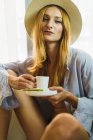Red hair woman in hat having cup of coffee and looking at camera — Stock Photo