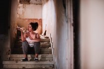 Молодая женщина сидит на лестнице выветрившегося дома и курит сигарету — стоковое фото