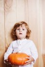 Confident child posing with pumpkin at wooden backdrop — Stock Photo