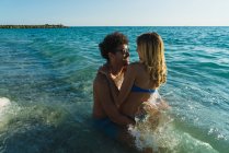 Casal em óculos de sol posando em ondas do oceano — Fotografia de Stock