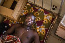 Benin, afrika - 31. august 2017: von oben betrachtet liegt ein mann im afrikanischen krankenhaus auf dem bett und blickt in die kamera — Stockfoto