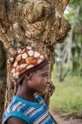 Бенин, Африка - 31 августа 2017 года: Вид сбоку на африканскую женщину со шрамами на лице, позирующую возле дерева — стоковое фото