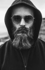 Retrato del hombre barbudo con gafas de sol y capucha - foto de stock